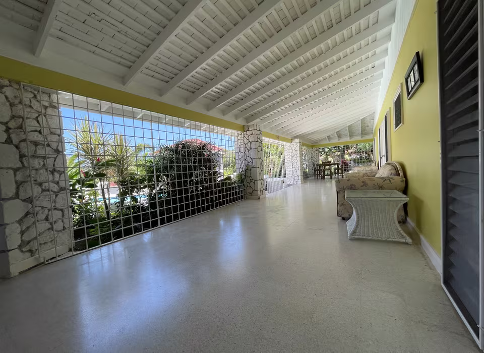 The verandah running the length of the house, wicker seating under a white beamed ceiling